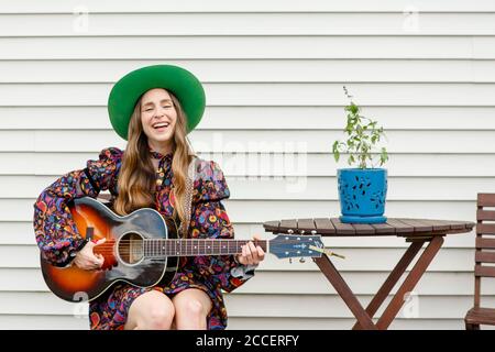 Une femme souriante s'assoit à une table extérieure jouant de l'acoustique guitare Banque D'Images
