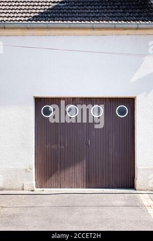 porte de garage en bois marron avec quatre fenêtres rondes en un bâtiment résidentiel avec façade en plâtre blanc Banque D'Images