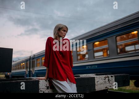 Une femme blonde dans une chemise rouge se tient près d'un train de passage Banque D'Images