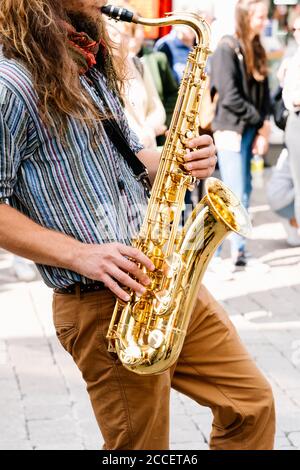 Photo verticale des mains d'un jeune homme avec les cheveux longs jouant au saxophone dans une rue bondée Banque D'Images