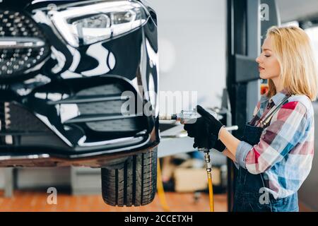 femme aux cheveux justes qui change de roue de voiture dans un atelier de réparation automobile. gros plan vue de côté. travail, profession Banque D'Images