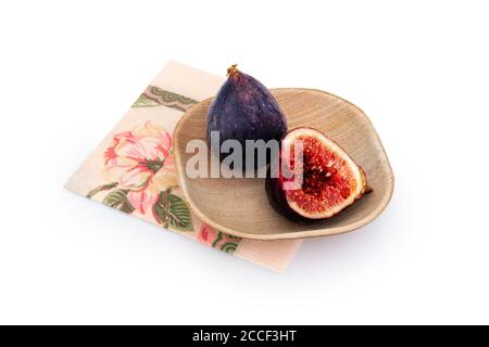 Figues mûres fraîches sur une assiette en bois avec une serviette décorative. Une figure est entière et l'autre est coupée en deux. Fruits de figuier méditerranéens sains sur un blanc Banque D'Images