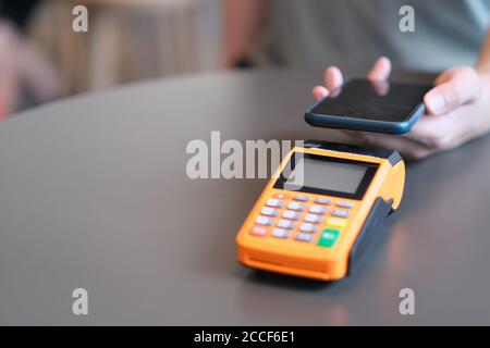 gros plan main tenant le smartphone par-dessus le terminal de pos sur la table. arrière-plan flou Banque D'Images