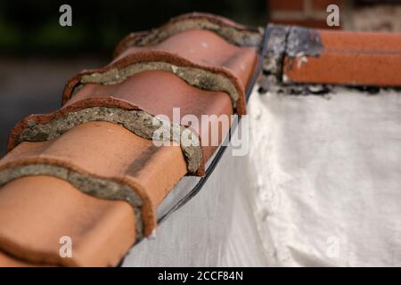 Carreaux de toit en terre cuite vieillissants avec des espaces remplis de mortier, recouvrant un mur de bâtiment, vu du toit. Banque D'Images