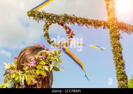 Jeune femme avec couronne de fleur sur arbre du milieu de l'été en Suède Banque D'Images