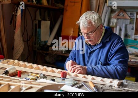 Homme senior qui fait l'aile en bois d'un avion radiocommandé sur le bureau de l'atelier, la construction de l'avion. Banque D'Images