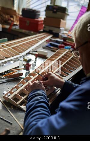 Homme senior fait l'aile en bois d'un avion radiocommandé sur le bureau de l'atelier, la construction de l'avion. Banque D'Images