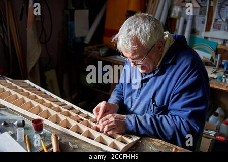 Homme senior fait l'aile en bois d'un avion radiocommandé sur le bureau de l'atelier, la construction de l'avion. Banque D'Images