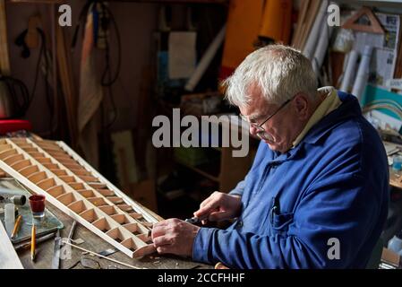 Homme senior fait l'aile en bois d'un avion radiocommandé sur le bureau de l'atelier, la construction de l'avion. Banque D'Images