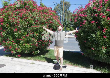 Un homme d'âge mûr agite ses bras entre deux grands arbustes aux fleurs roses Banque D'Images