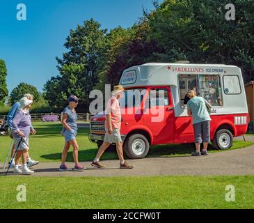 Femme achetant de la crème glacée auprès d'un vendeur dans une vieille fourgonnette Bedford, avec des personnes âgées marchant sous le soleil d'été. Rutland Water, Normanton, Angleterre, Royaume-Uni. Banque D'Images