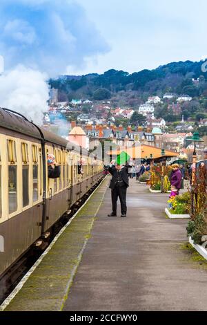 Un garde agite le drapeau vert pour autoriser un train à vapeur à partir de la gare de Minehead, West Somerset Railway Spring Gala event, Angleterre, Royaume-Uni Banque D'Images