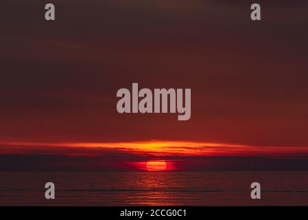 le moment du coucher du soleil quand le soleil touche l'horizon, camouflage derrière de minces nuages et coloration de l'eau rouge Banque D'Images