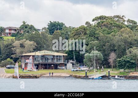 Deux personnes regardent un petit bateau à voile qui quitte le rivage au Hunters Hill Sailing Club dans le port de Sydney, en Australie Banque D'Images