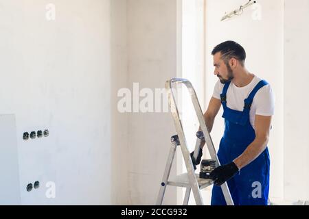 Le constructeur a mis le niveau laser sur l'échelle et regarde les marques sur le mur Banque D'Images