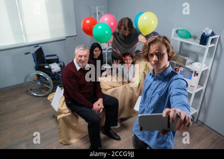 Un garçon fait des visages tout en prenant un selfie avec sa petite sœur malade et toute la famille. Banque D'Images