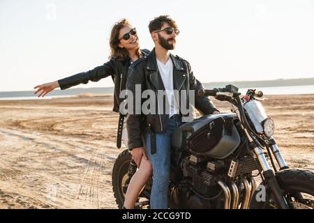 Couple de yong béatiful portant des vestes assis sur une moto à la plage ensoleillée Banque D'Images