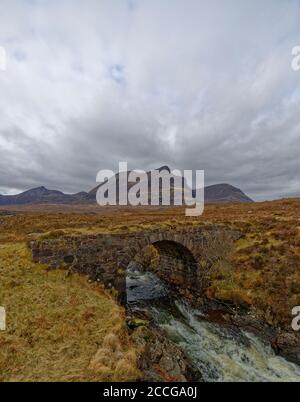 L'eau qui coule rapidement traverse une arche de l'ancien pont de Stone Road, avec des montagnes en arrière-plan lors d'une journée humide en avril dans les Highlands. Banque D'Images