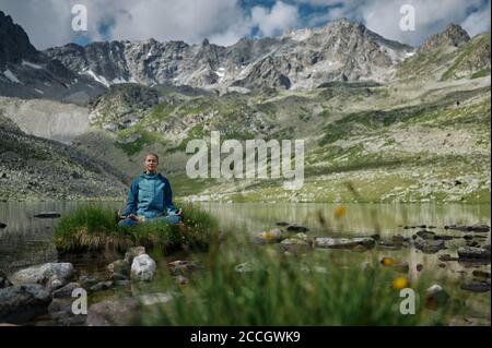 La jeune femme est assise en position de yoga lotus contre le lac turquoise dans les montagnes. Une fille de randonneur extrême se repose dans la nature sauvage. Style de vie trekking. D Banque D'Images