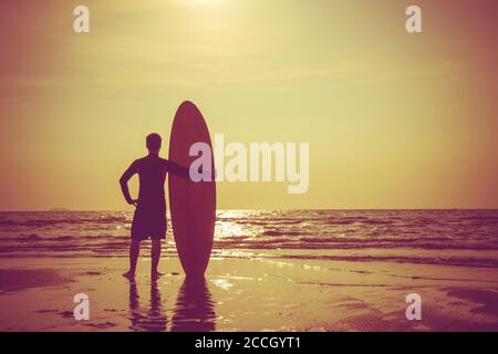 Silhouette d'homme de surf debout avec une planche de surf. Surf sur la plage au coucher du soleil. Sports nautiques en plein air aventure style de vie.activité d'été. Belle Asie homme Mo Banque D'Images