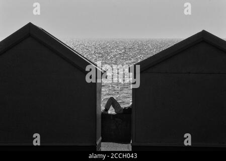 Un homme allongé sur le mur de la mer, près des cabanes de plage de Brighton, chalets, East Sussex, Angleterre, Royaume-Uni Banque D'Images