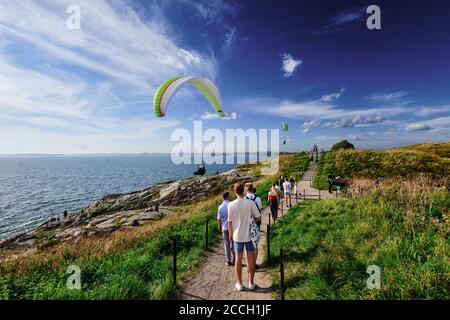 Helsinki, Finlande - 15 août 2020 : les gens marchent sur l'île de Suomenlinna lors de la chaude journée d'été. Les parapentes glissent le long de la côte de l'île. Banque D'Images