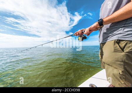 Pêche à la roue de canne homme pêche à partir d'un bateau de pêcheur en Floride. Port de la technologie portable de la montre intelligente pour le sport en extérieur Banque D'Images