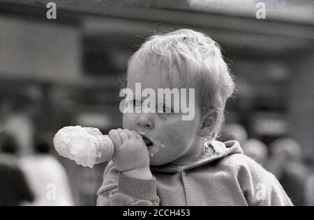 Joyeux bébé garçon, manger un double cornet de cachets de glace ou de cône, en commençant par le bas et pas le haut! Angleterre, années 1980. Banque D'Images