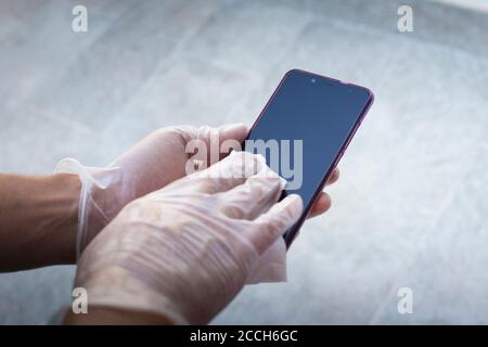 Mains avec des gants jetables sur l'écran du smartphone, en essuyant l'écran avec un chiffon blanc. Banque D'Images