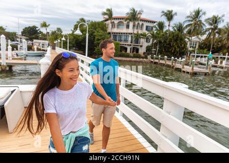 Joyeux jeune décontracté couple touristes marchant sur la promenade de Floride à Marina appréciant la journée d'été tenant les mains. Relation interraciale asiatique fille