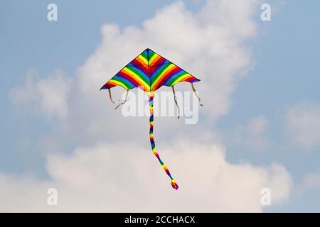 Cerf-volant préféré des enfants par temps venteux au printemps, ciel bleu et nuages blancs. Un cerf-volant coloré oscille dans le vent. Banque D'Images