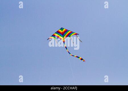 Cerf-volant préféré des enfants par temps venteux au printemps, ciel bleu et nuages blancs. Un cerf-volant coloré oscille dans le vent. Banque D'Images