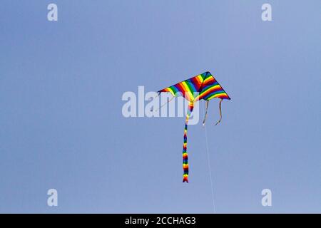 Cerf-volant préféré des enfants par temps venteux au printemps, ciel bleu et nuages blancs. Un cerf-volant coloré oscille dans le vent. Banque D'Images