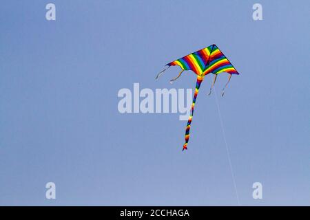 Cerf-volant préféré des enfants par temps venteux au printemps, ciel bleu et nuages blancs. Un cerf-volant coloré oscille dans le vent. Banque D'Images