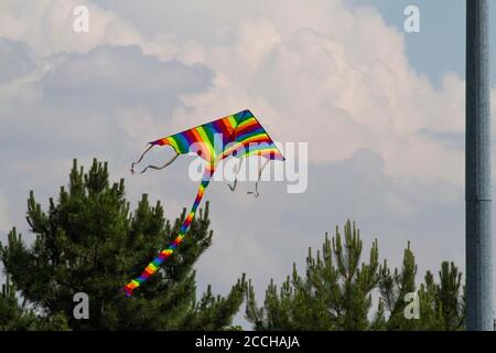 Cerf-volant préféré des enfants par temps venteux au printemps, ciel bleu et nuages blancs. Un cerf-volant coloré oscille dans le vent. Banque D'Images