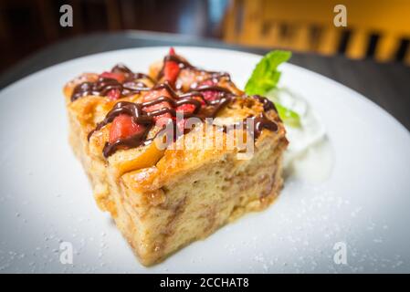 Une assiette blanche avec une tranche de pain fraîchement cuit pouding recouvert de fraises et arrosé de chocolat Banque D'Images