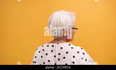 Vue arrière d'une femme sénior à cheveux gris isolée sur fond orange. Photo de haute qualité Banque D'Images