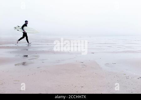 Surfez ! Un surfeur traverse une épaisse brume de mer vers la mer Banque D'Images