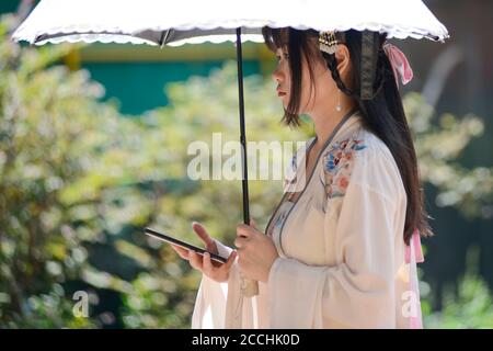 Une jeune fille chinoise vêtue de vêtements traditionnels et d'un parapluie, et tenant son téléphone portable. Jianghan Road, Wuhan, Chine Banque D'Images