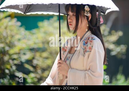 Une jeune fille chinoise vêtue de vêtements traditionnels et d'un parapluie, et tenant son téléphone portable. Jianghan Road, Wuhan, Chine Banque D'Images