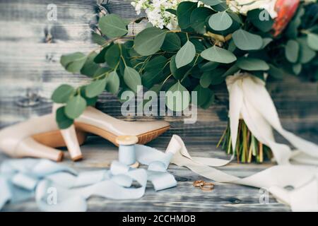 Anneaux de mariage en or sur une base en bois avec des chaussures de mariée beige, une bobine de ruban et un bouquet de fleurs. Banque D'Images