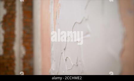 master applique du mastic blanc sur un mur et se marapport avec un couteau à mastiquer dans une salle de rénovation de la maison en journée. Stuc blanc sur le mur. Mise Banque D'Images