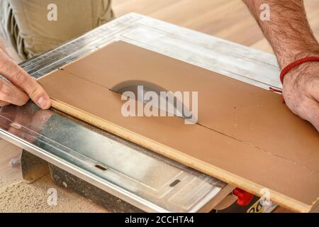 Homme coupant des planches de plancher stratifié sur la scie circulaire, détail sur les mains tenant le panneau en bois et l'anneau rotatif, photo d'illustration d'amélioration de la maison Banque D'Images
