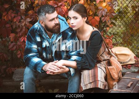 Jeune couple assis à l'extérieur dans le parc d'automne. Style de vie, famille heureuse par beau temps. Fille et barbu gars ou heureux amoureux tenant les mains et la hug Banque D'Images