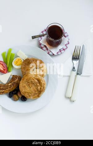 Pâtisserie traditionnelle turque « Boyoz » dans une assiette avec bagel au sésame, œuf, olives et tomates en tranches, petit déjeuner en blanc avec thé Banque D'Images