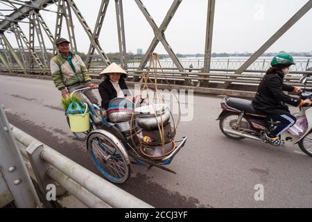 Hue / Vietnam - 20 janvier 2020: Femme vietnamienne avec chapeau conique traditionnel sur tricycle chargé avec des têtes de fournitures de cuisine pour monter la nourriture de rue Banque D'Images