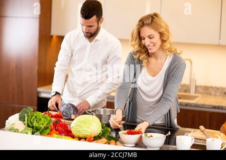 Voir l'jeune homme à aider son amie dans la cuisine cuisine moderne Banque D'Images