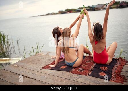 Jeunes filles attrayantes en bikini de boire de la bière sur la côte du lac par temps ensoleillé Banque D'Images