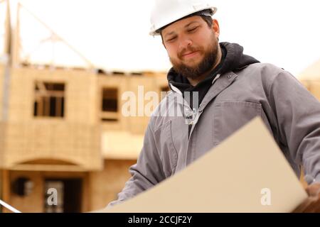 Portrait du constructeur regardant le plan de dessin architectural sur papier au chantier de construction. Banque D'Images