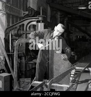 Dans les années 1950, un homme d'âge moyen et historique en combinaison dans un atelier de transport ou dans un grand hangar de Great Wester Railways faisant du métal, Angleterre, Royaume-Uni. Banque D'Images